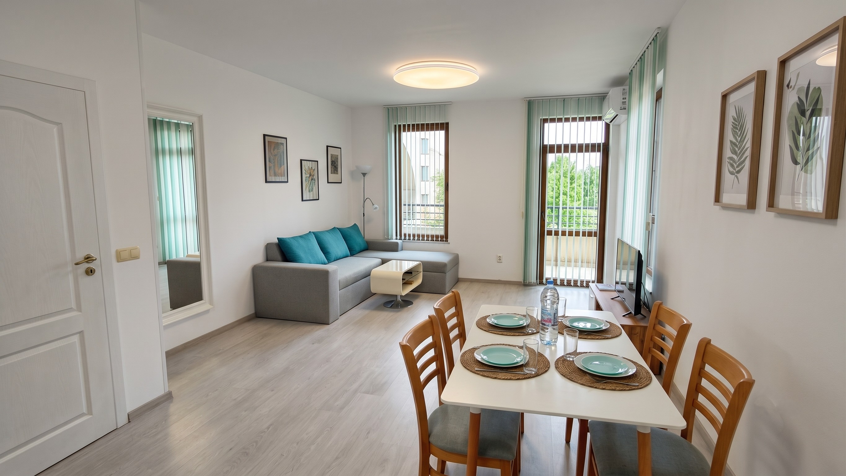 Bright living room with kitchen table, four chairs, a sofa and a TV.
