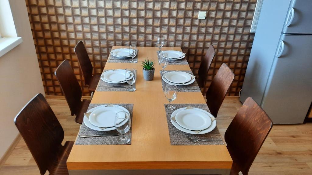 Wooden dining table set for six with white plates and wine glasses, surrounded by chairs.